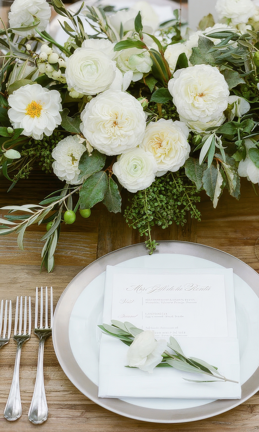 Elegant wedding table arrangement, featuring olive foliage and pastel flowers, matching our sage green and pastel boutique dresses.