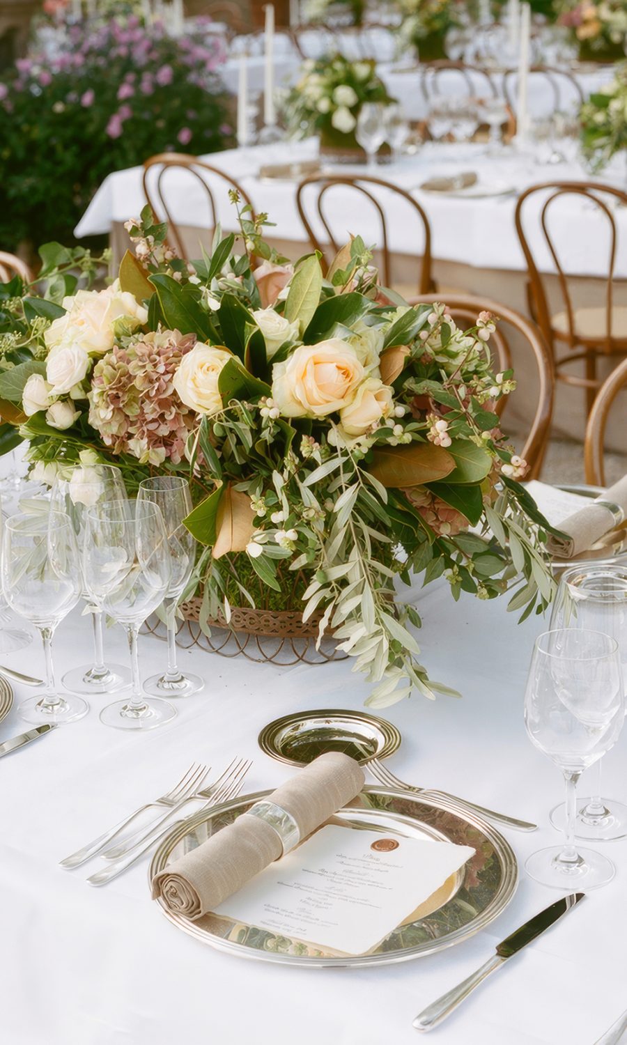 Lush floral wedding table arrangement featuring warm apricot and pastel blooms with olive foliage, acting as a floral anchor for mismatched bridesmaid dresses.