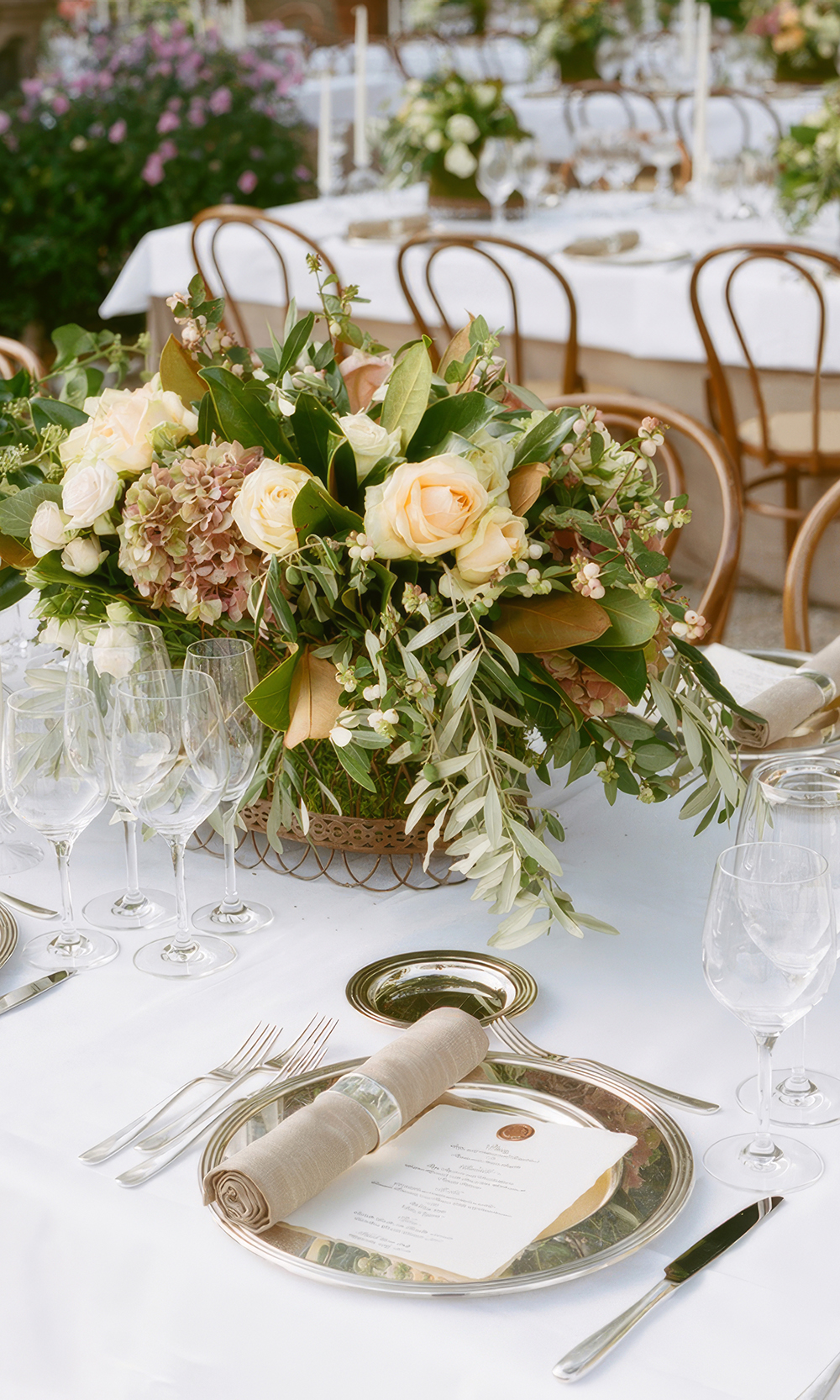 Lush floral wedding table arrangement featuring warm apricot and pastel blooms with olive foliage, acting as a floral anchor for mismatched bridesmaid dresses.