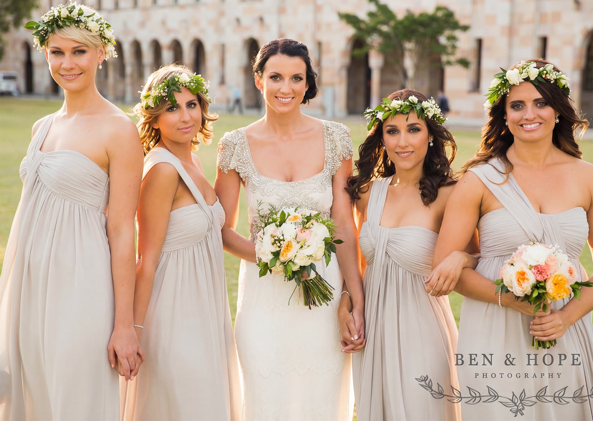 Beautiful bride posing with her four bridesmaids wearing our flowing grey one-shoulder dresses.