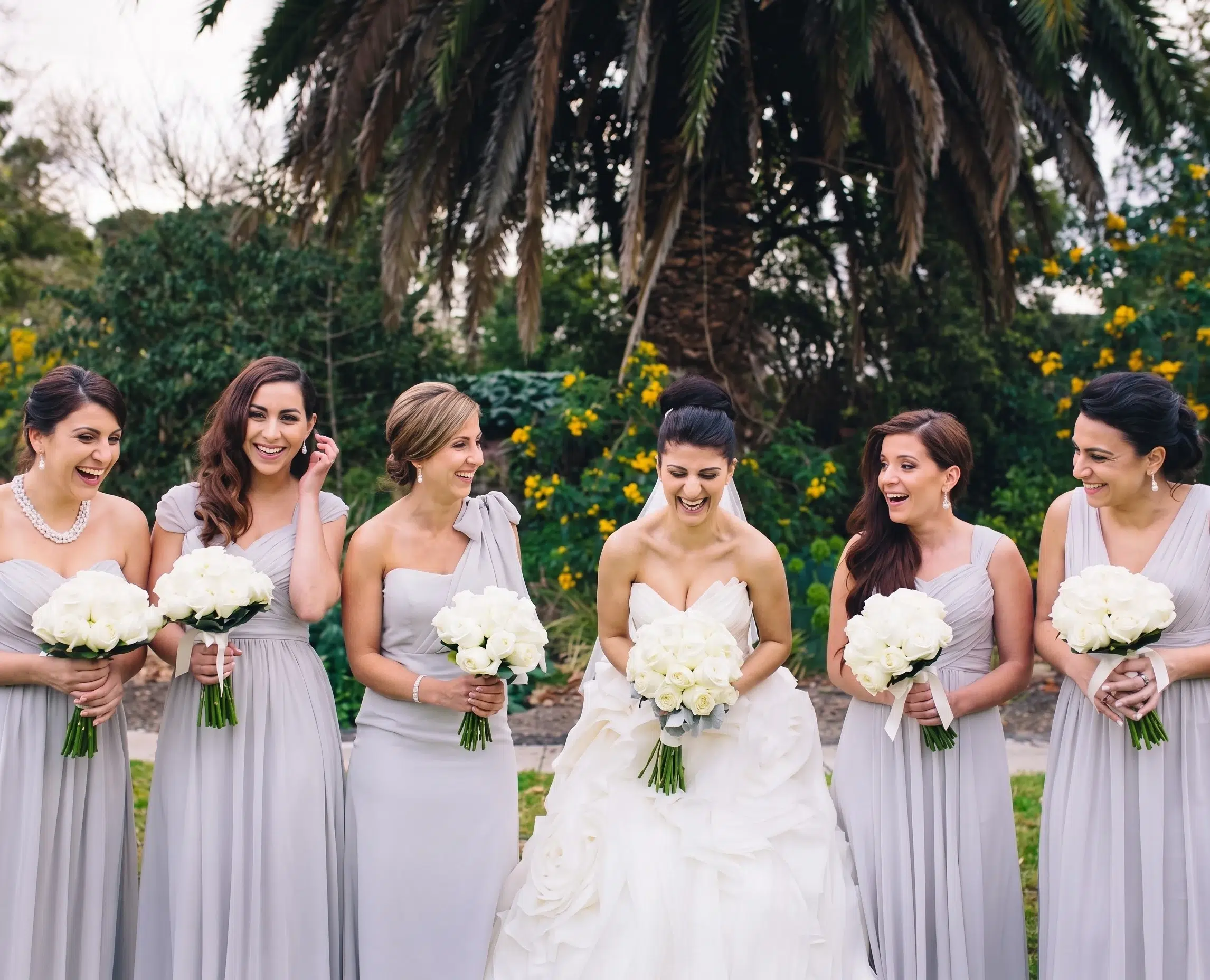 A real bridal party wearing mix and match bridesmaid dresses by Natasha Millani. Bridesmaid dresses are made from exactly same colour chiffon, but have various neckline designs. Dresses are unified by matching florals.